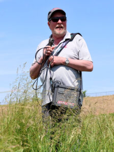 Michael Neff in a field with a microphone and speaker while leading a tour of the WSU grass breeding farm.