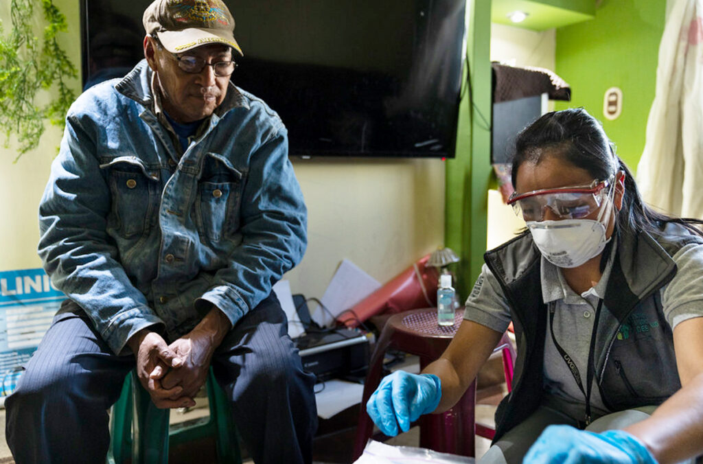 A field researcher prepares to collect a sample from a participant seated on a stool.