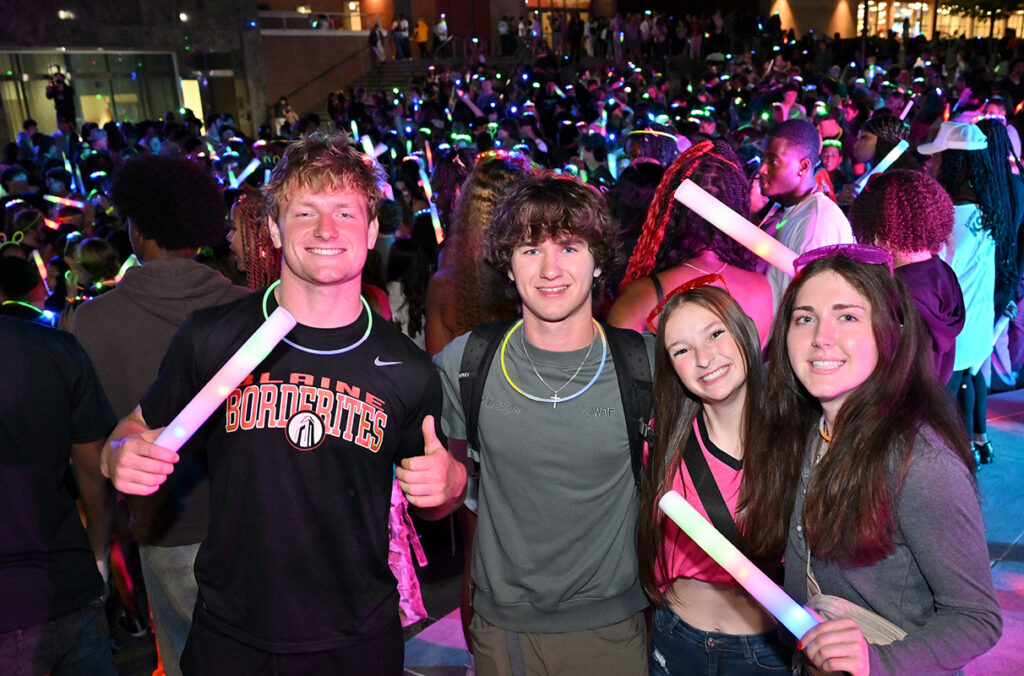 Four students pose for a photo with glow sticks and other items at the CougGlow Dance Party.
