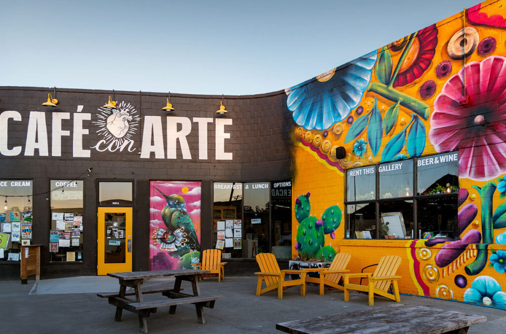 Adirondack chairs and picnic tables sit underneath a mural painted outside Café con Arte.