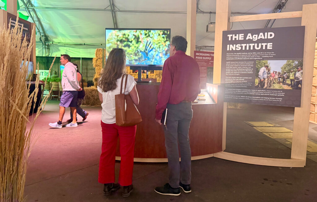 Two people watch a video presentation as part of a display about the AgAID Institute.