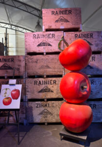 A display featuring stacks of apple crates and a sculpture with three giant apples stacked on top of each other.