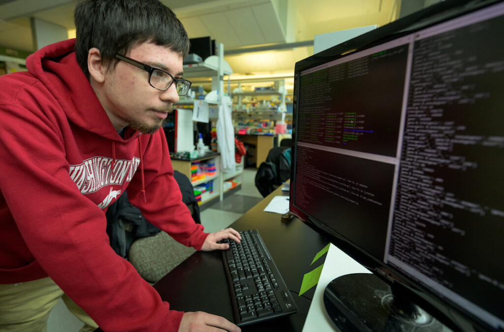 Sam Toompas leaning in front of a computer work station examining data.