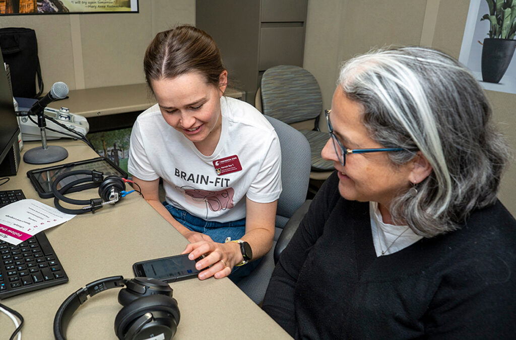Graduate student Hannah Tjelle sitting at a desk with a BRAIN FIT participant examining a smartphone.