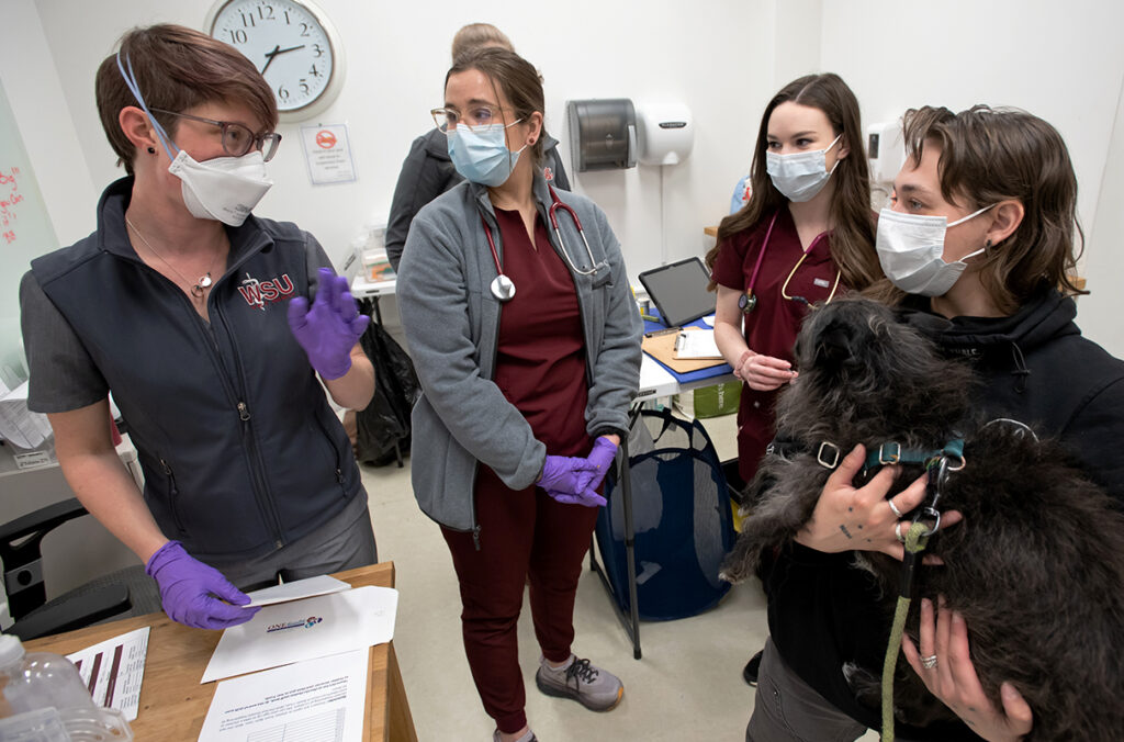 A WSU associate professor and two veterinary medicine students speak to a pet owner holding a dog.