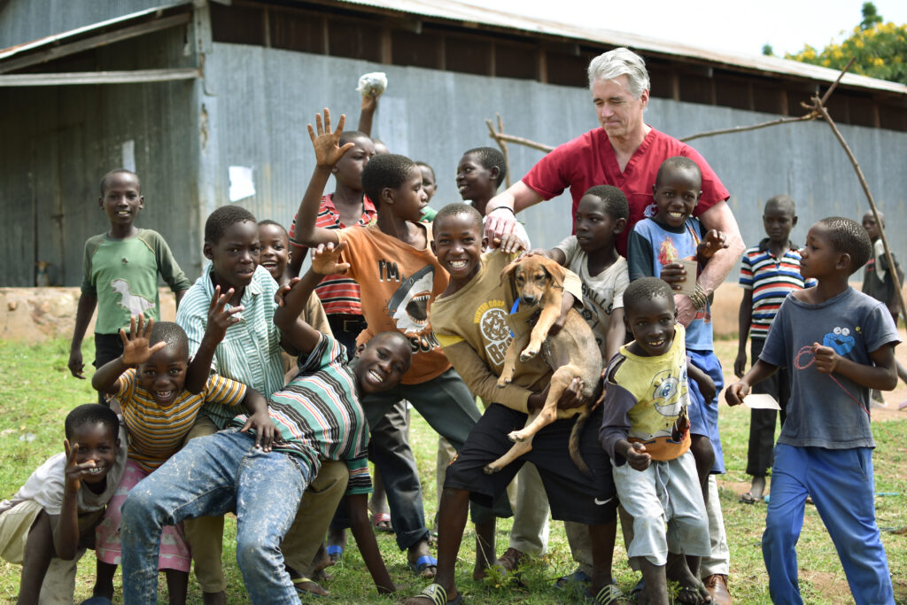 WSU's Guy Palmer is shown with a group of young children and a dog playing in front of him during a visit to Tanzania.