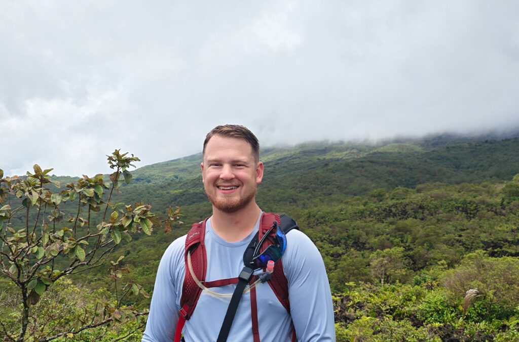 Closeup of John Balke standing in front of a forest covered mountain in Costa Rica.