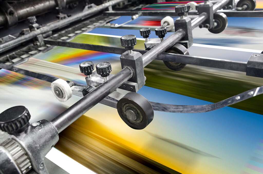 Paper with colored ink running through a commercial printing press.