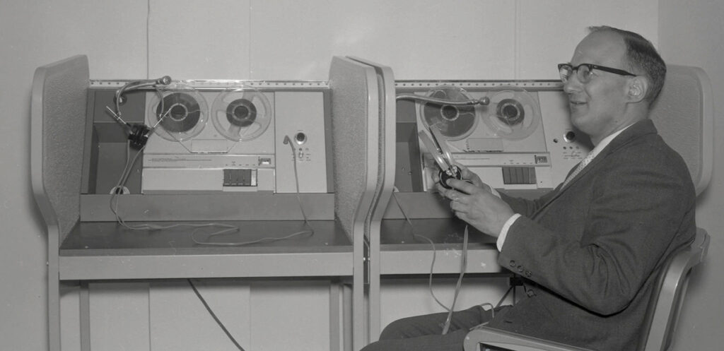 A man uses an audio tape recorder in a black and white photo from 1963.