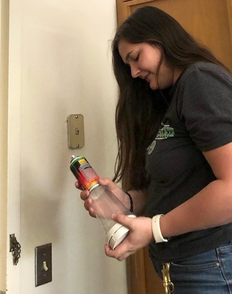 Maci Brantner holding a can of smoke and a smoke alarm as she tests it.