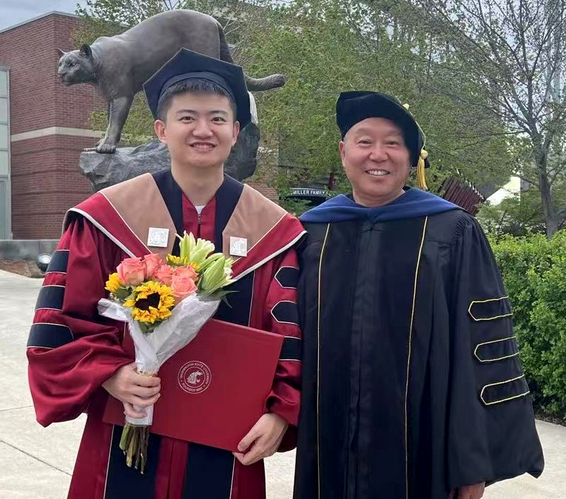 A professor and graduate student pose in front of the Cougar Pride statue on the Pullman campus following commencement.
