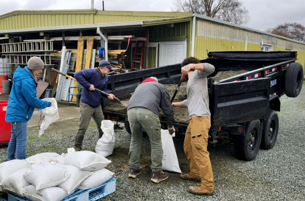 Four WSU employees making sandbags behind a dump trailer full of sand.