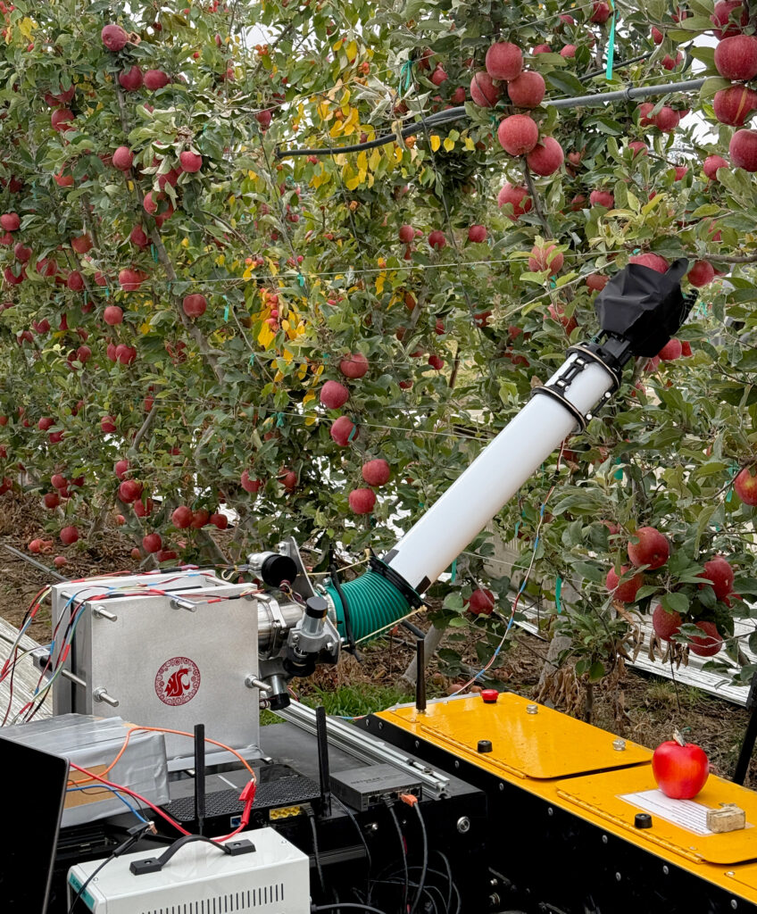 A robotic arm picks apples in an orchard.