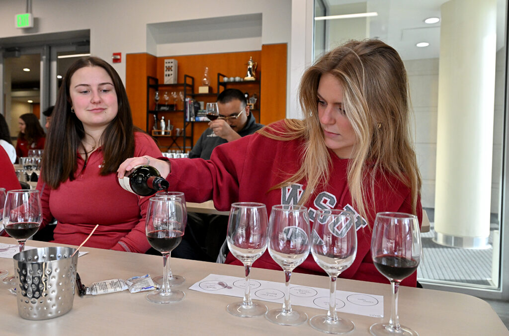 A WSU student pours red wine into glasses while another student looks on in the Beverage Lab.
