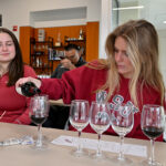 A WSU student pours red wine into glasses while another student looks on in the Beverage Lab.