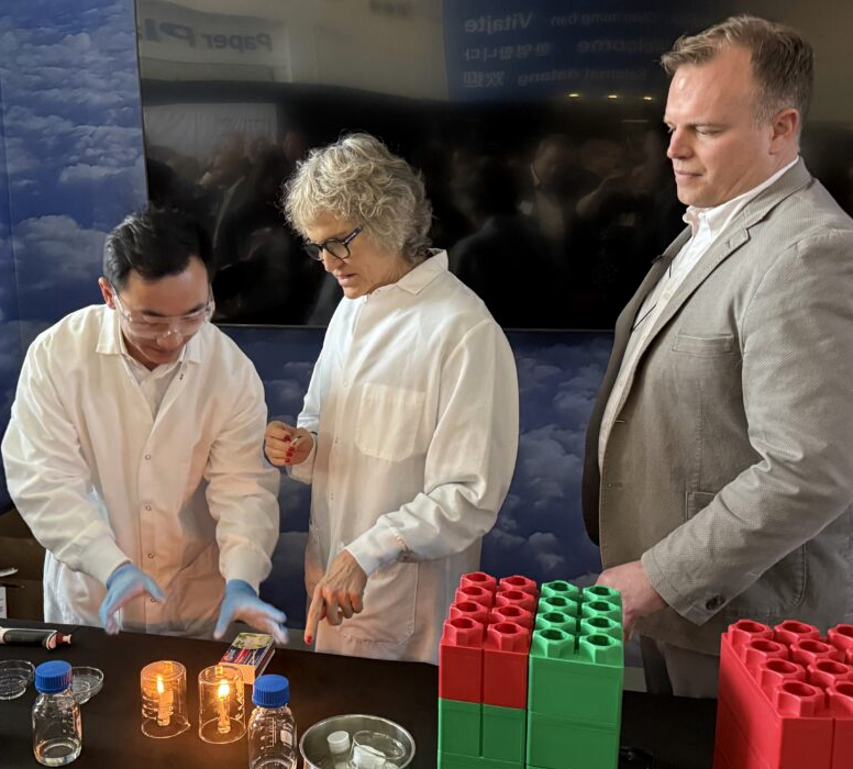 Betsy Cantwell, Harrison Yang, and Josh Heyne standing behind a table demonstrating sustainable aviation fuel.
