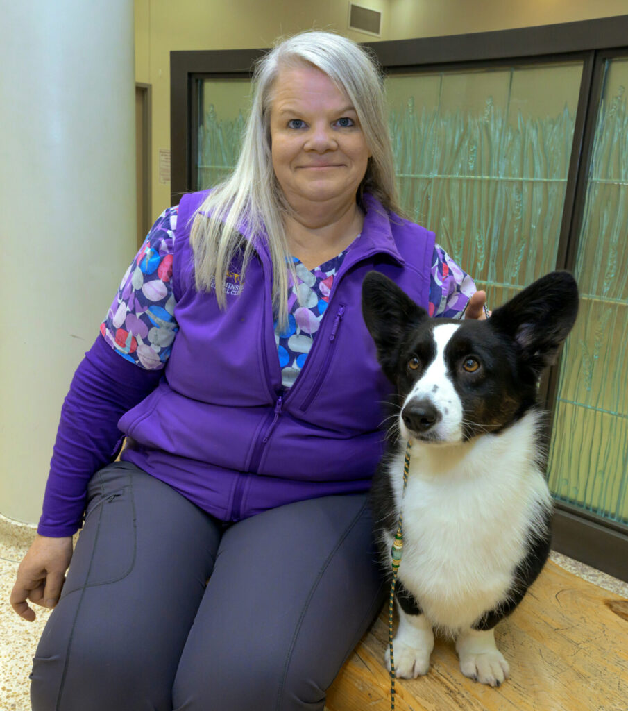 Denise Waiting sitting with her corgi dog, Witton, on a wooden bench.