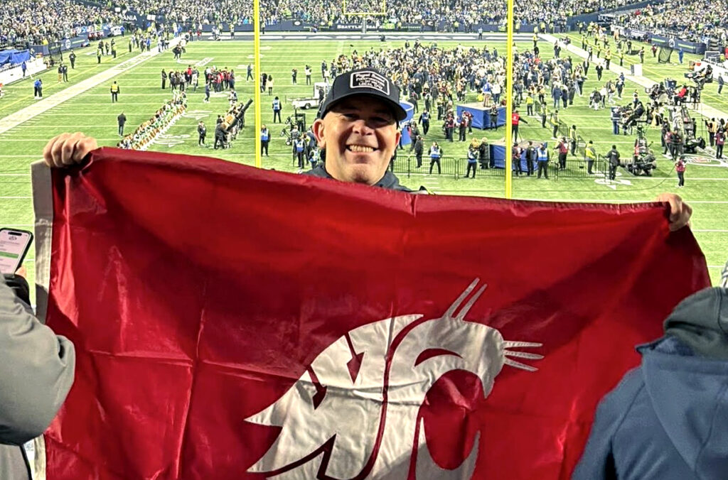 WSU alumnus Jason Fox holding a Cougar flag at a Seattle Seahawks football game.