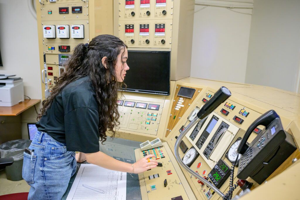 A student employee working the Nuclear Science Center control desk with many dials and instruments.
