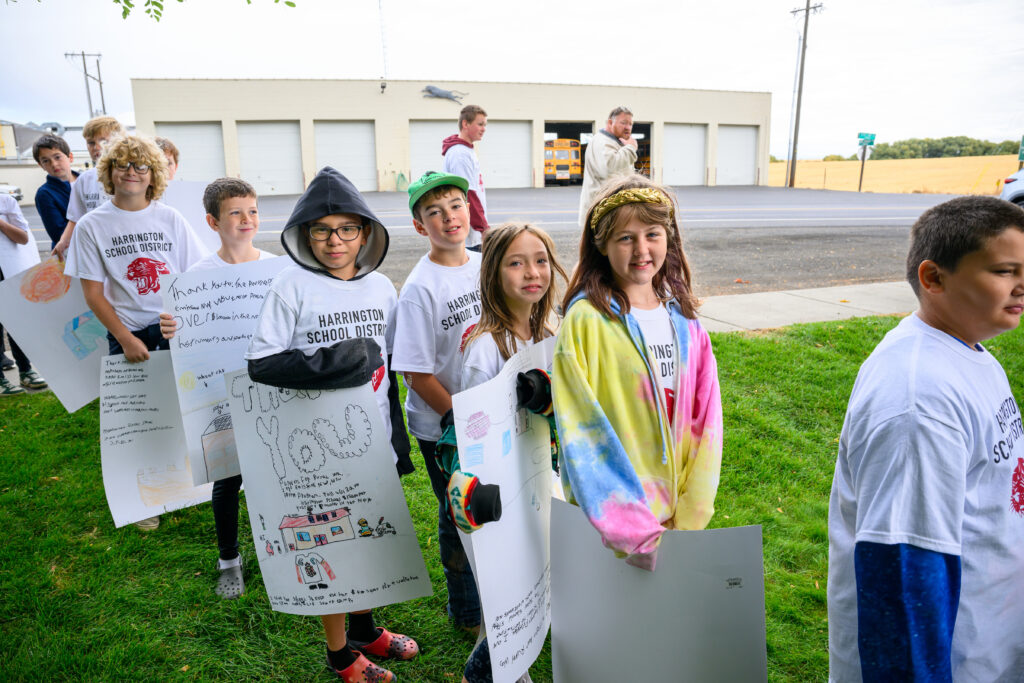 Children smiling outside their school and holding signs saying thank you for their school's solar panels.