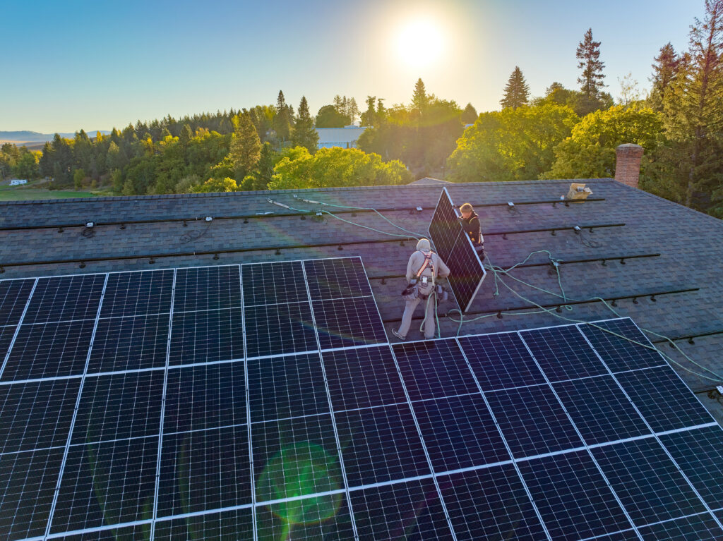 Two people installing solar panels on a roof as the sun rises.