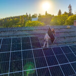 Two people installing solar panels on a roof as the sun rises.