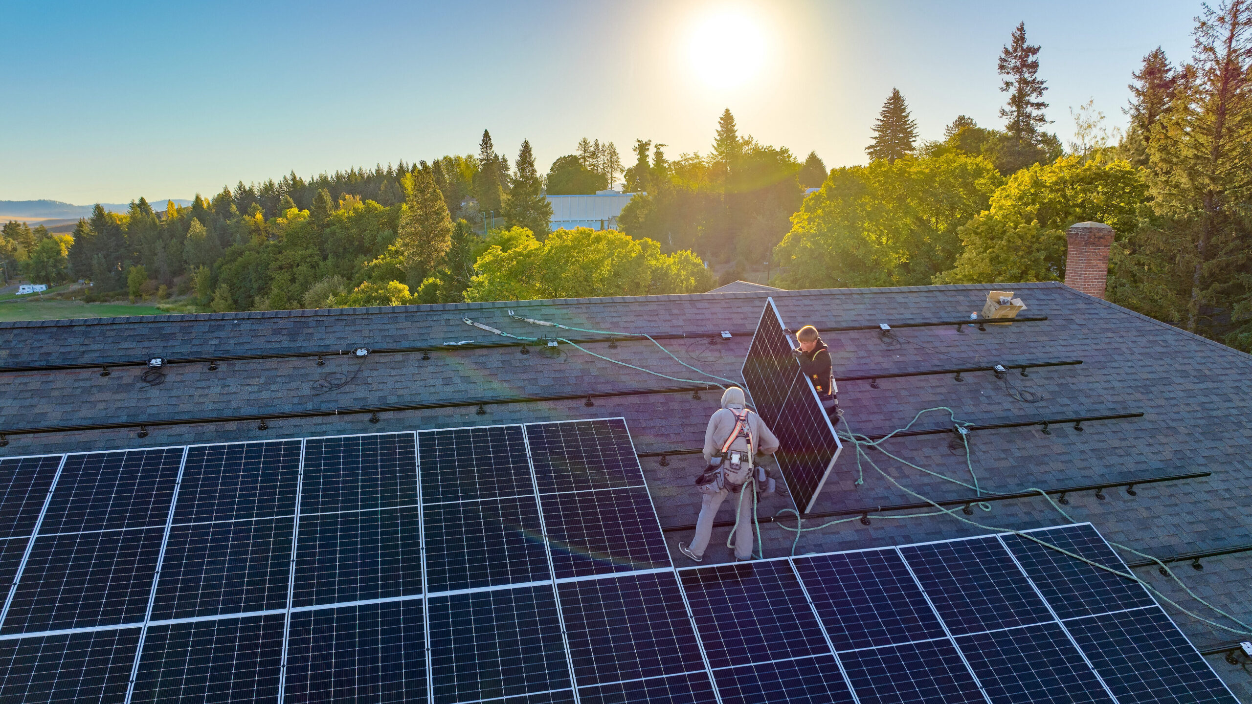 Two people installing solar panels on a roof as the sun rises.