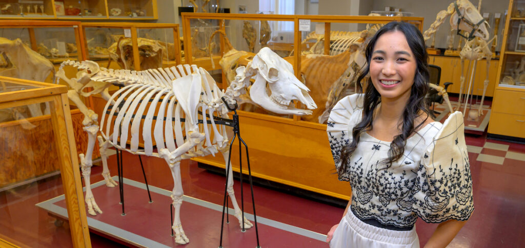 Anjelica Bautista standing next to a display of several animal skeletons.