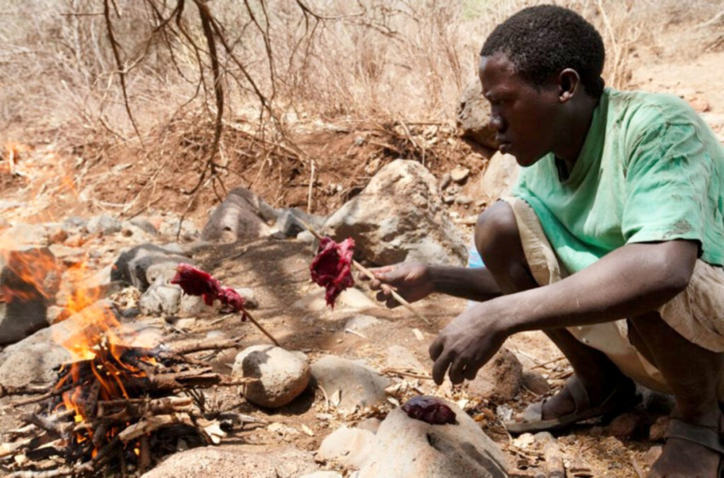 A Hadza man in Tanzania cooks over an open fire.