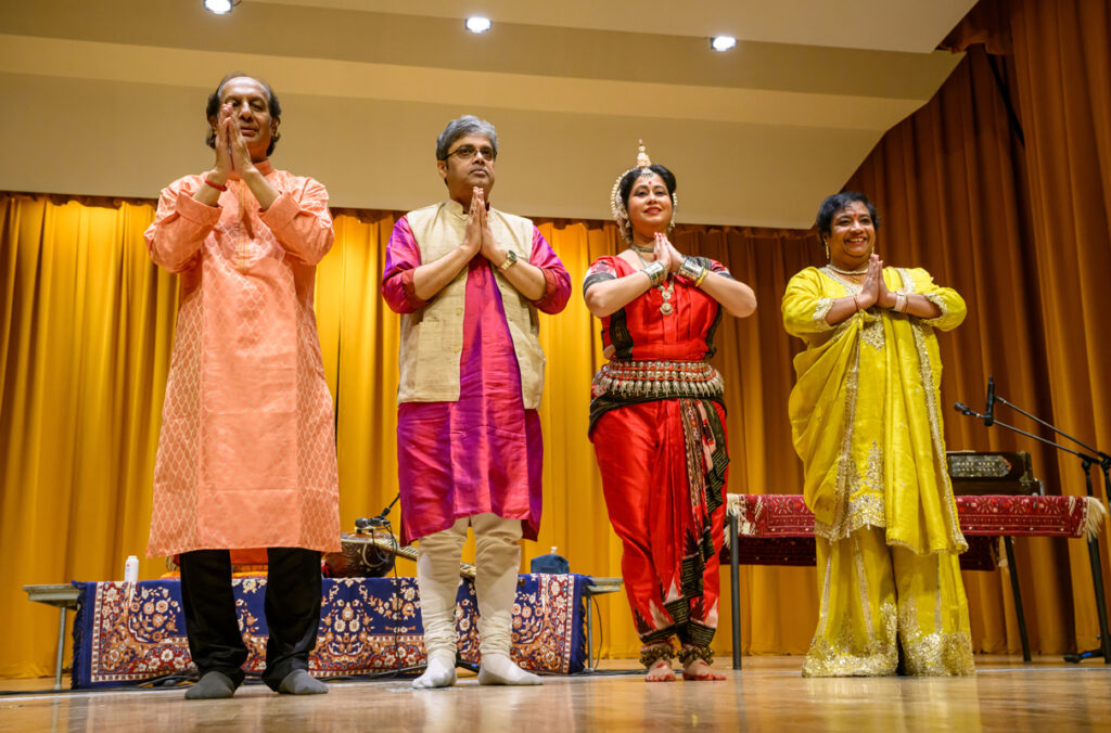 Three musicians and a dancer standing on stage during a North Indian classical music and dance concert.