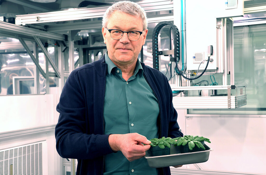 Professor Helmut Kirchhoff holding a tray of small plants in a lab.