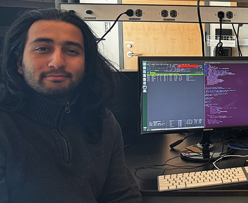 Ishparsh Uprety sitting next to a computer in a lab.
