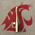 A baseball, a torpedo bat, and a traditional baseball bat laid on a floor featuring a WSU logo.