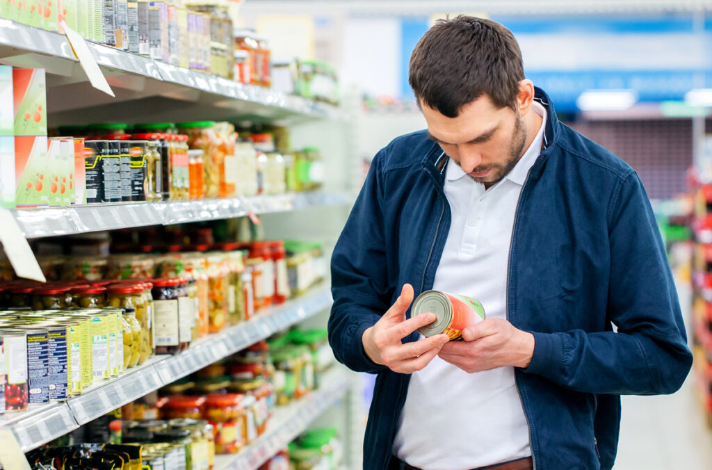 A man holding a can of food in a supermarket as he examines the label.