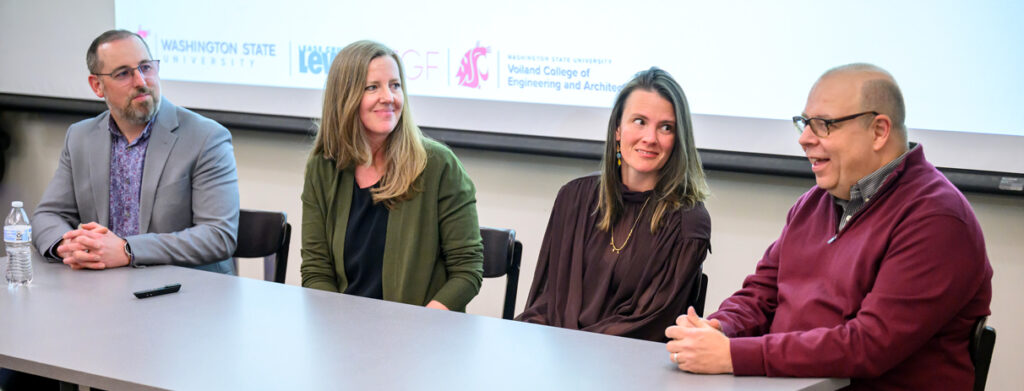 Four panelists sitting at a table as one of the four speaks to an audience.