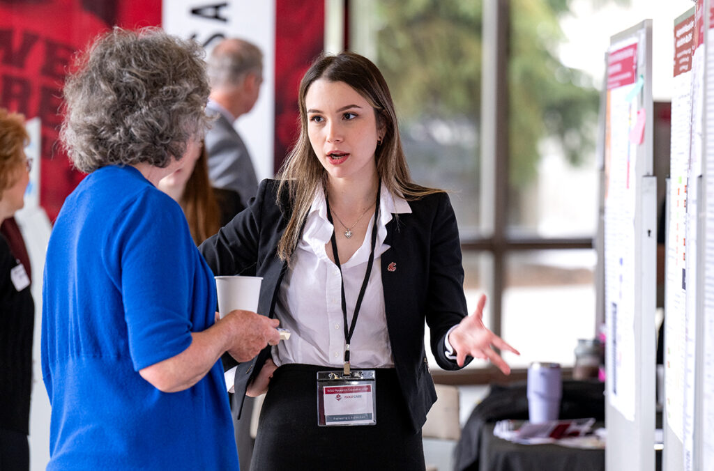 A WSU student speaks to a judge while standing next to research poster on a bulletin board.