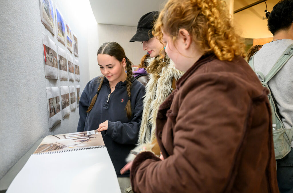 Three students looking at a design book while visiting a gallery exhibition.