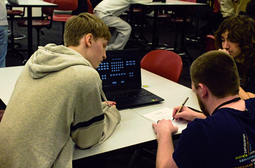 Three hackathon participants sit around a table and collaborate on a project.