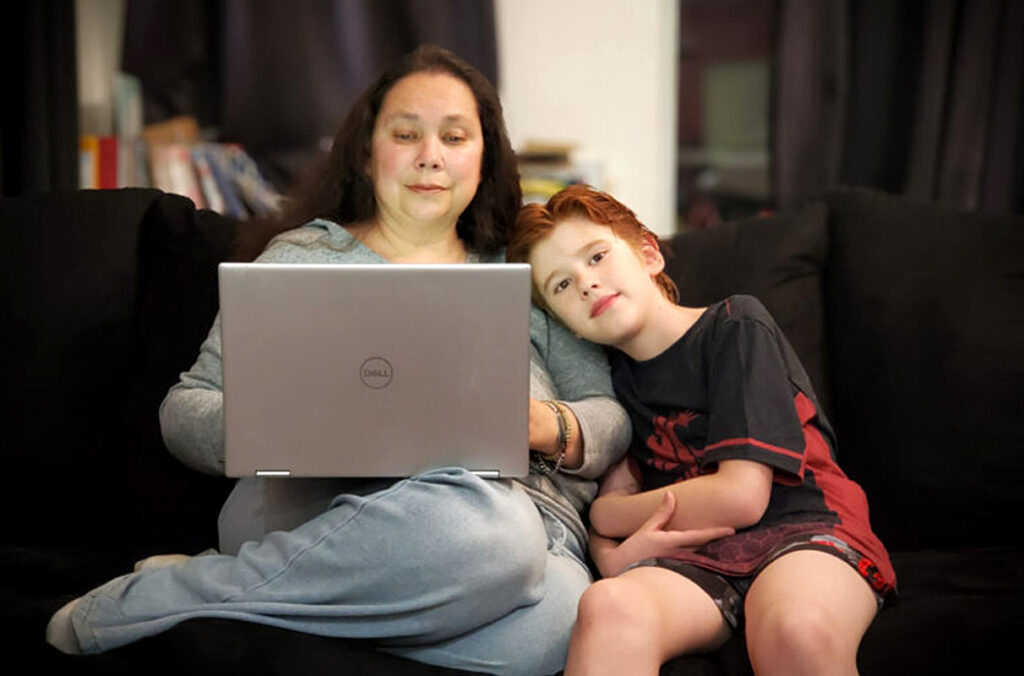Aunjelique Andersen working on a laptop computer while her son sits next to her on a couch.