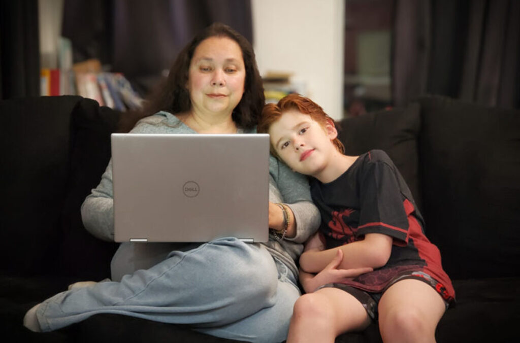 Aunjelique Andersen works on a computer while her son sits next to her.