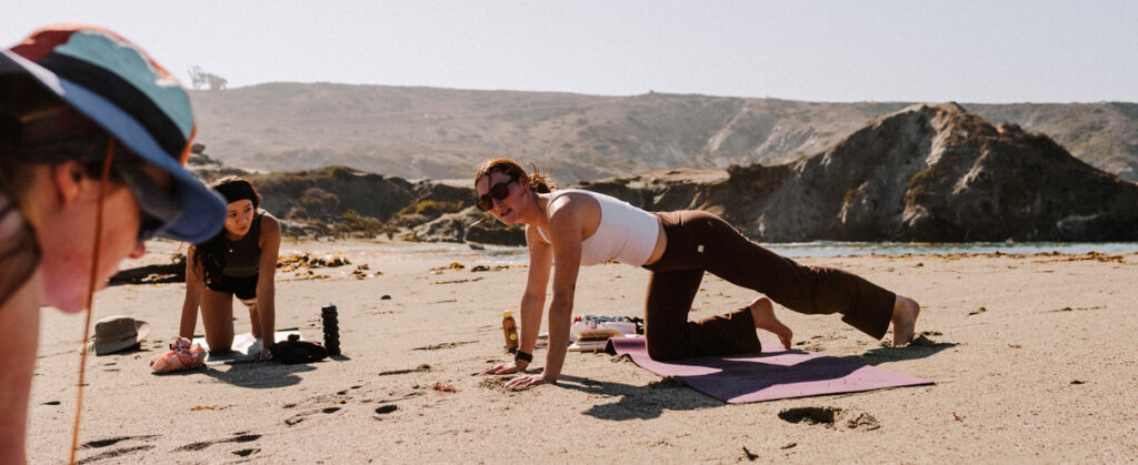 A group of women performing yoga on a beach.