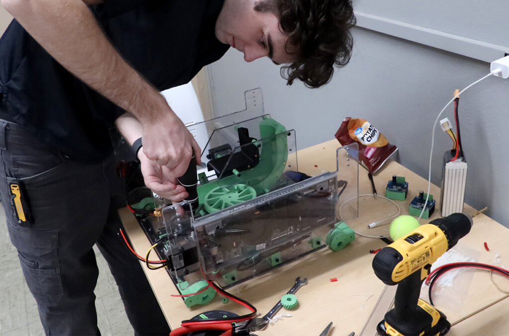 A hackathon participant using tools to work on computerized hardware components.