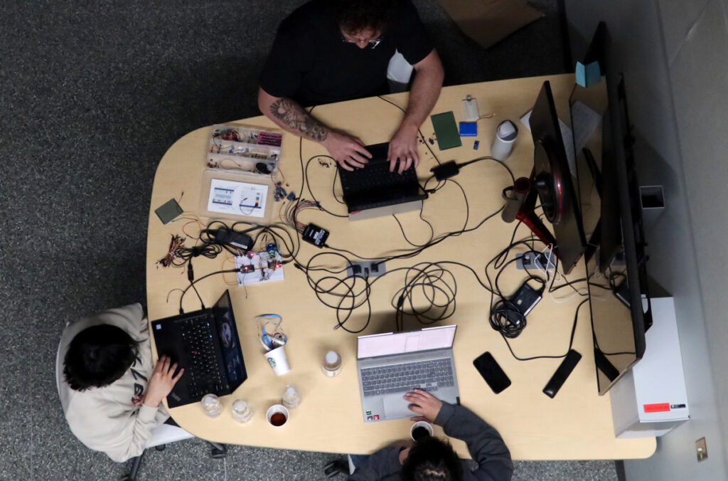 An overhead view of three hackathon participants working on laptop computers at a table.