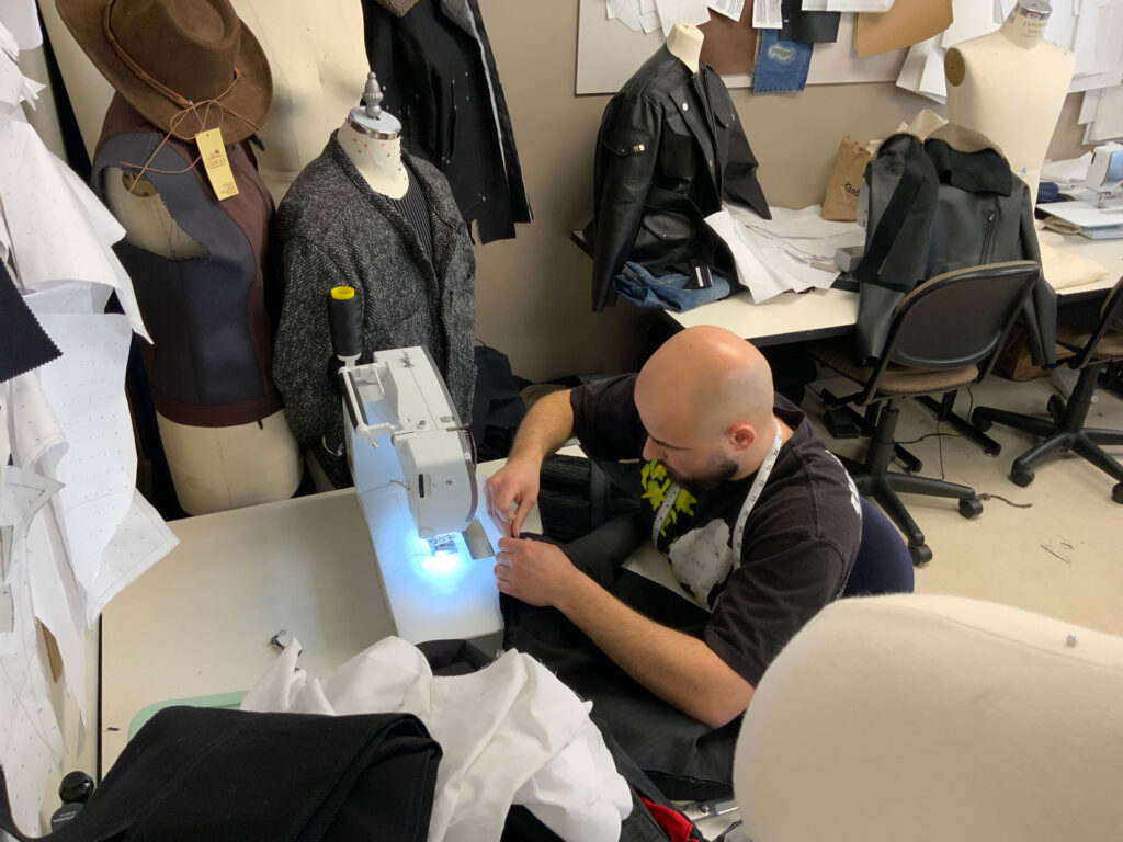 Kamil Hall bends over a sewing machine, working on his design for the AMDT Fashion Show.