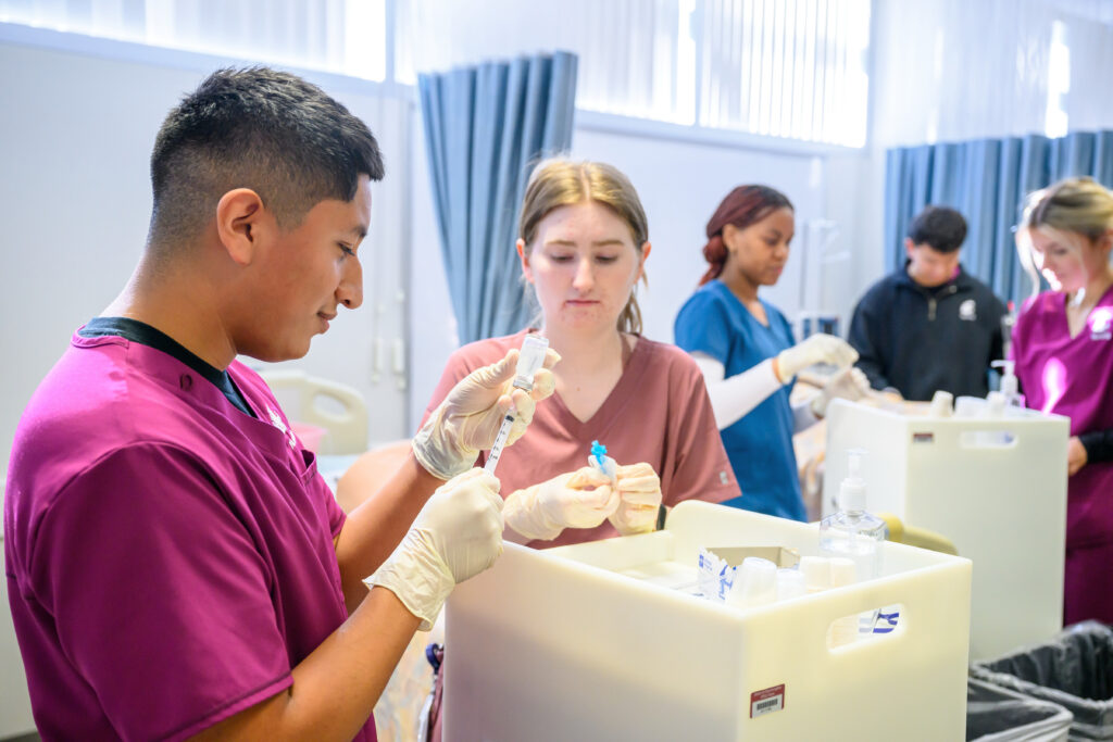 A student filling an injection needle from a bottle while others work in the background.