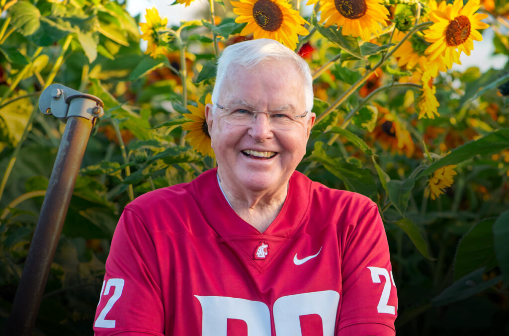 Sam Hunt wearing a WSU Cougars football jersey and standing in a field of sunflowers.