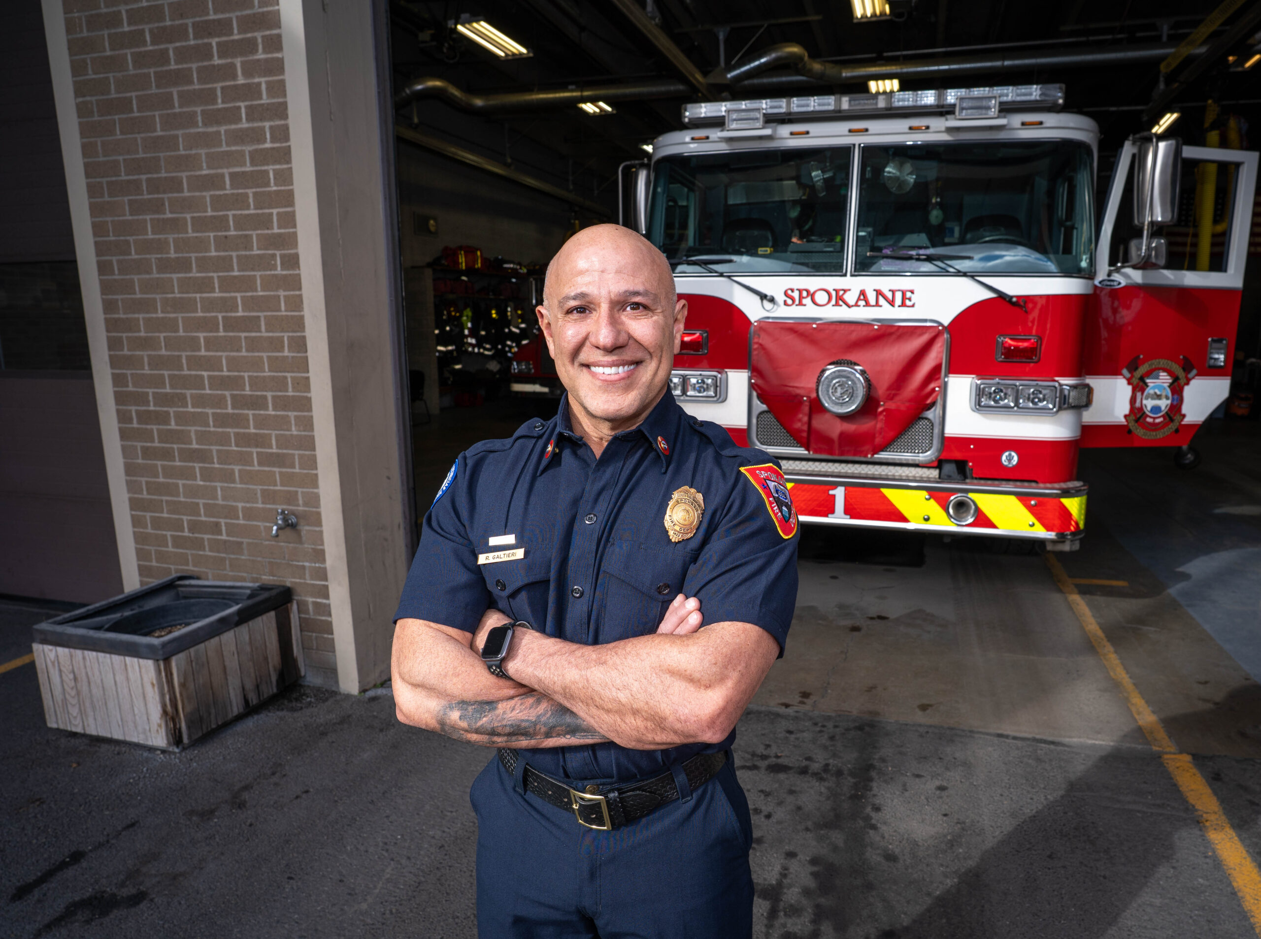 Rich Galtieri in a blue uniform, smiling with arms crossed in front of a Spokane fire truck.