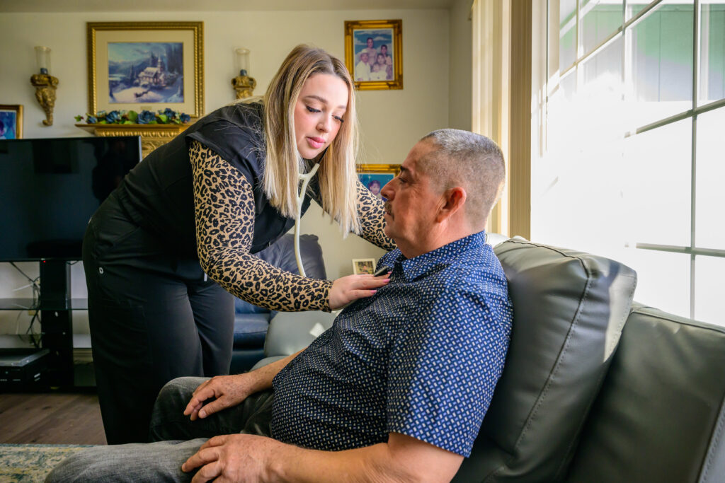 A WSU nursing student listening to a patient's heart with a stethoscope in their home.