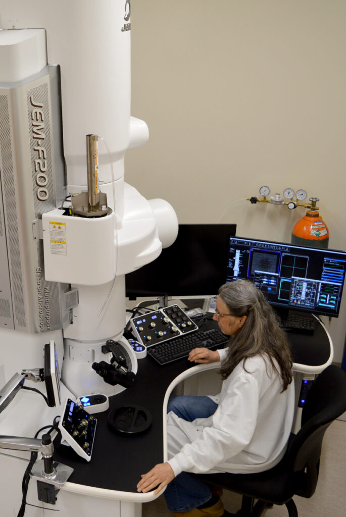 Valerie Lynch-Holm sitting at a workstation for a transmitting electron microscope.