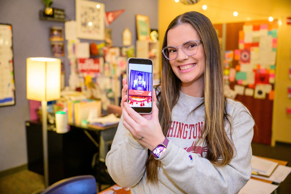 A smiling person holding their global campus graduation photo on their phone.